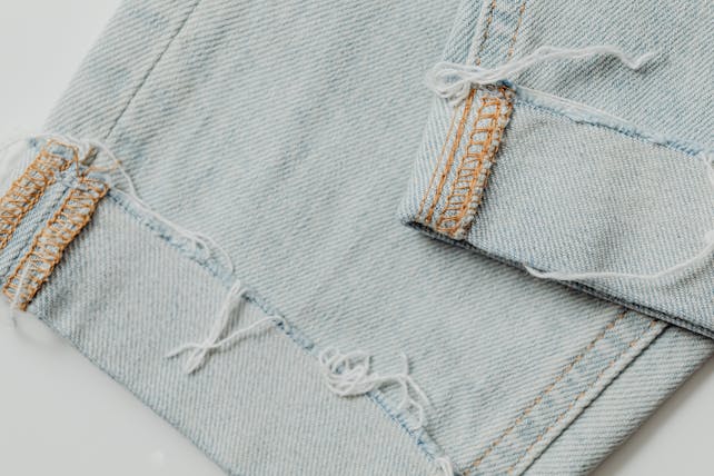A detailed close-up shot of frayed light blue denim fabric displaying intricate stitching and texture.